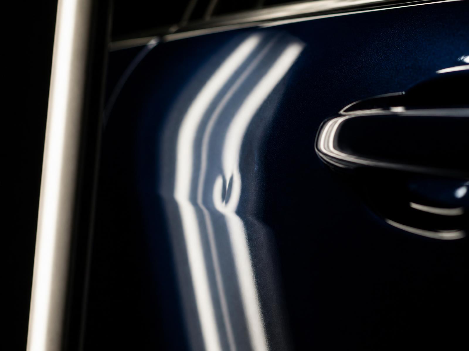 Macro view of reflection lines bending across impact damage in a painted panel