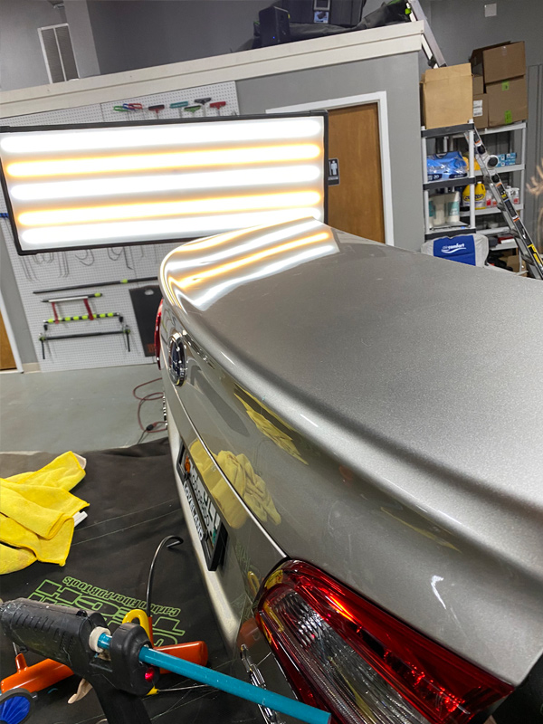 Hail damage on a vehicle trunk lid read under reflective shop lighting